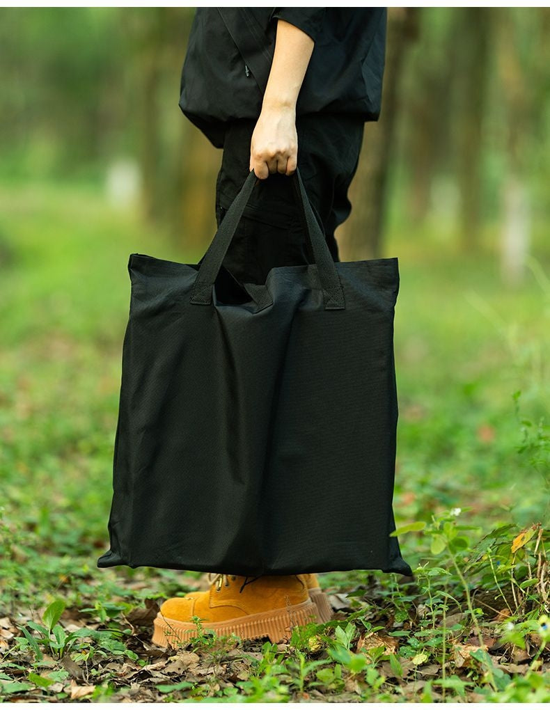 Person trägt die schwarze Aufbewahrungstasche des faltbaren Campingtisches auf einem Waldweg